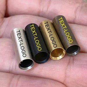 May include: Four metal tubes in silver, black, gold, and bronze. Each tube has the text "TEXT-LOGO" printed in yellow. The tubes are cylindrical with a hollow interior.