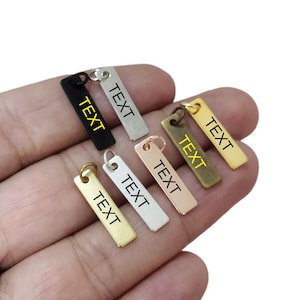 Può includere: Sei etichette metalliche di forma rettangolare con angoli arrotondati. Le etichette sono di diversi colori: nero, argento, oro, oro rosa e ottone. Ogni etichetta ha un foro nella parte superiore per essere attaccata a un portachiavi o ad un altro oggetto. La parola "TESTO" è incisa su ogni etichetta.