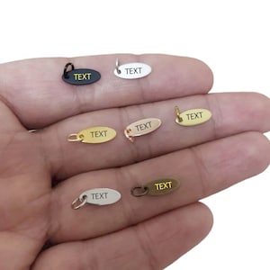 May include: Six oval-shaped metal tags with a hole for a jump ring. The tags are in different colours: black, silver, gold, rose gold, and two shades of brass. Each tag has the word "TEXT" engraved on it.