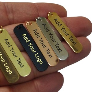 May include: Six metal tags in different finishes, including gold, silver, black, and rose gold. Each tag has a rectangular shape and is engraved with the text "Add Your Text" or "Add Your Logo".