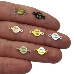 Può includere: Sei etichette rotonde in metallo con anelli a salto. Ogni etichetta è incisa con il testo "Your Logo". Le etichette sono di diversi colori: oro, argento, nero e due tonalità di oro.