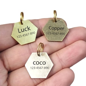 May include: Three gold-colored hexagonal dog tags with black engraved text. The tags read "Luck 123-4567-890", "Copper 123-4567-890", and "Coco 123-4567-890".