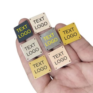 May include: Six square metal tags with rounded corners and four holes. The tags are in different colors: gold, silver, black, and two shades of brown. Each tag has the text "TEXT LOGO" printed in yellow.