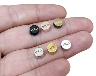 May include: Six round metal charms with the word "LOGO" printed on them. The charms are in different colours: black, gold, silver, rose gold, and bronze.