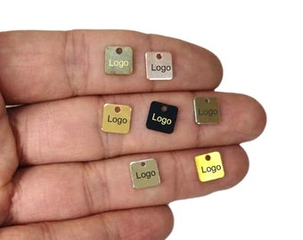 Può includere: Sei etichette metalliche quadrate con un foro nella parte superiore. Le etichette sono di diversi colori: oro, argento, nero e ottone. Ogni etichetta ha la parola "Logo" stampata.