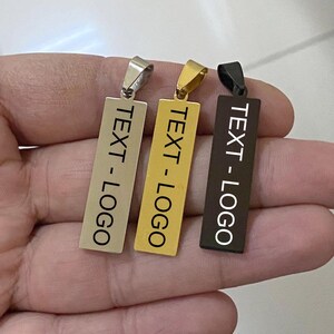 May include: Three rectangular pendant necklaces in silver, gold, and black. Each pendant has the text "TEXT - LOGO" printed in a contrasting colour. The pendants are displayed against a neutral background.