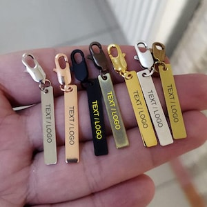 Puede incluir: Siete llaveros de metal plateado, dorado y negro con una etiqueta rectangular que dice "TEXT / LOGO".