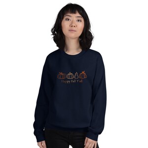 May include: Navy blue sweatshirt featuring an orange outline of four pumpkins. The text "Happy Fall Y'all" is printed below the pumpkins. The sweatshirt is a long-sleeved crew neck.