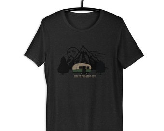 以下が含まれることがあります： キャンプをテーマにしたグラフィックが特徴の濃いグレーのTシャツ。デザインには、トレーラー、山、木、そして「I HATE PULLING OUT」というテキストが含まれています。Tシャツは黒いハンガーに掛けられています。