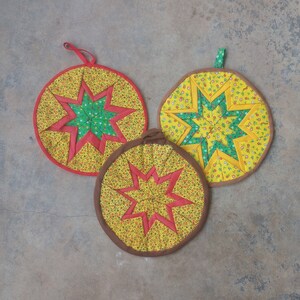 May include: Three round yellow, green, and red fabric pot holders with a star design. The pot holders have a brown fabric border.