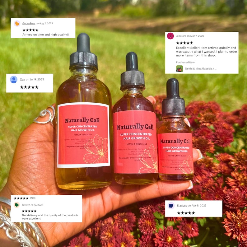 K&ouml;nnte beinhalten: Drei Flaschen Naturally Cali Super Concentrated Hair Growth Oil mit Tropfapplikatoren. Die Flaschen haben rote Etiketten mit wei&szlig;em Text und einem floralen Design. Die Flaschen werden in einer Hand vor einem Hintergrund aus roten Blumen gehalten.