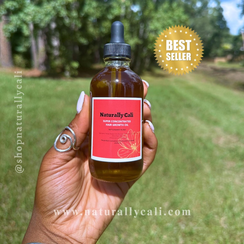 K&ouml;nnte beinhalten: Eine klare Glasflasche mit Haarwuchs&ouml;l und einem schwarzen Tropfaufsatz. Die Flasche hat ein rotes Etikett mit wei&szlig;em Text, auf dem "Naturally Cali Super Concentrated Hair Growth Oil" steht. Im Hintergrund befindet sich ein goldener "Best Seller"-Aufkleber.