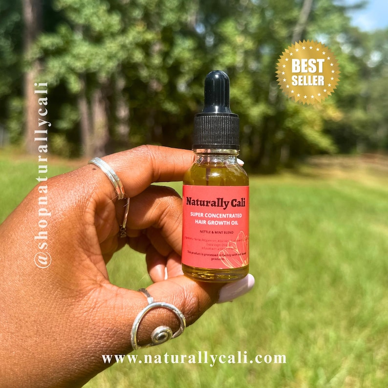 K&ouml;nnte beinhalten: Eine kleine Glasflasche mit Naturally Cali Super Concentrated Hair Growth Oil, gehalten in einer Hand. Die Flasche hat eine schwarze Pipette und ein rotes Etikett mit wei&szlig;em Text. Ein goldener "Best Seller"-Aufkleber befindet sich im Hintergrund. Die Website ist www.naturallycali.com.