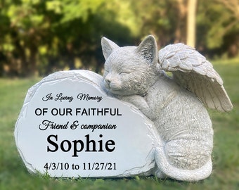 May include: White ceramic memorial statue of a sleeping cat with angel wings. The statue is resting on a heart-shaped stone with the inscription "In Loving Memory Of Our Faithful Friend & Companion Sophie 4/3/10 to 11/27/21".