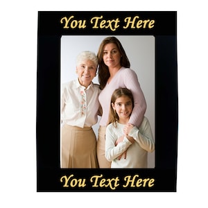 Puede incluir: Marco de fotos negro con una inscripción dorada que dice "You Text Here" en la parte superior e inferior. El marco contiene una foto de tres generaciones de una familia: una abuela, una madre y una niña. Las mujeres sonríen y miran a la cámara.