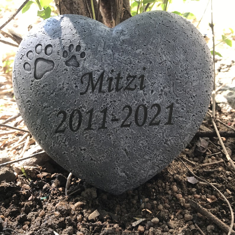 May include: A grey heart-shaped stone memorial with two paw prints and the inscription "Mitzi 2011-2021".
