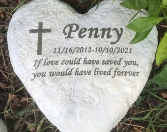 May include: White heart-shaped stone memorial with a cross and the name Penny inscribed on it. The dates 11/16/2012-10/10/2021 and the inscription "If love could have saved you, you would have lived forever" are also engraved on the stone.