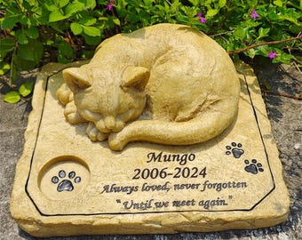 May include: A beige cat-shaped memorial stone with the name "Mungo" and dates 2006-2024. The inscription reads "Always loved, never forgotten" and "Until we meet again." Paw prints and a circular paw print design are also present.