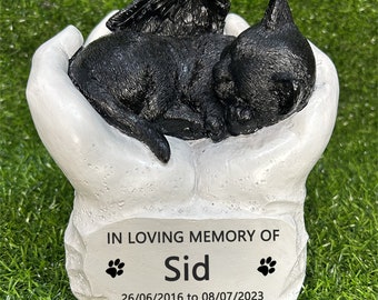 May include: White ceramic memorial with a black kitten with wings sleeping in a pair of hands. The base has a plaque that reads "In loving memory of Sid 26/06/2016 to 08/07/2023" with paw prints on either side of the name.