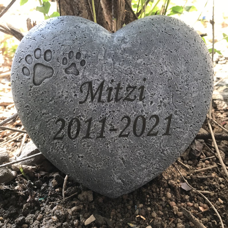 May include: Grey heart-shaped stone memorial with two paw prints and the inscription "Mitzi 2011-2021".