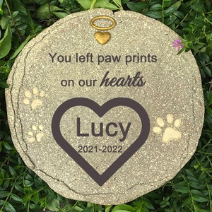 Op de afbeelding: Een grijs stenen gedenkteken met de tekst "You left paw prints on our hearts" en een hart met de naam "Lucy" en de data "2021-2022".