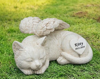 May include: White ceramic cat memorial statue with angel wings and a heart-shaped plaque that reads "Kitty 2012-2024".