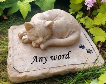 May include: A stone memorial with a sleeping cat sculpture and the words "Any word" inscribed on it. The memorial is surrounded by green grass.