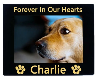 May include: Black wooden photo frame with a gold inscription "Forever In Our Hearts" and a paw print on either side of the name "Charlie" in gold. The frame holds a photo of a golden retriever.
