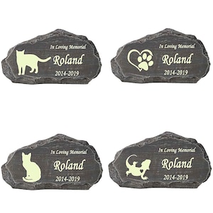 K&ouml;nnte beinhalten: Vier graue Stein-Gedenkmarker f&uuml;r Haustiere mit dem Namen Roland und den Daten 2014-2019. Jeder Marker zeigt eine andere Tiersilhouette: eine Katze, eine Pfote in einem Herzen, eine Katze und ein Eidechse.