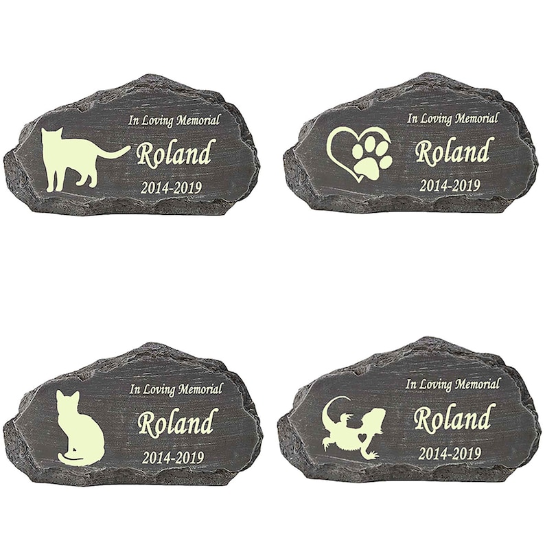 K&ouml;nnte beinhalten: Vier graue Stein-Gedenkmarker f&uuml;r Haustiere mit dem Namen Roland und den Daten 2014-2019. Jeder Marker zeigt eine andere Tiersilhouette: eine Katze, eine Pfote in einem Herzen, eine Katze und ein Eidechse.
