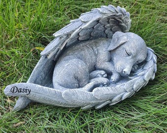 May include: A gray puppy sculpture sleeping peacefully within feathered angel wings. The sculpture is set on a bed of green grass. The word "Dasiy" is written on the base of the sculpture.
