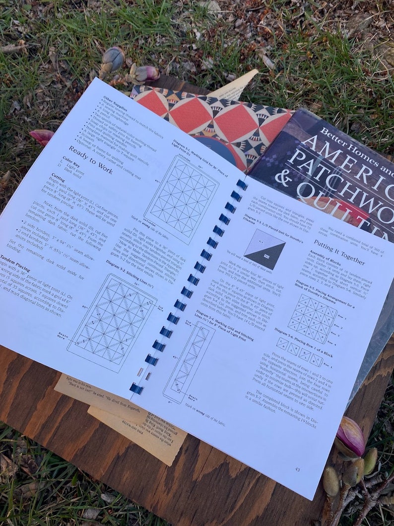 Pode incluir: Um close-up de um livro intitulado "Better Homes and American Patchwork & Quilting" com uma p&aacute;gina aberta em uma se&ccedil;&atilde;o sobre "Colocando tudo junto". A p&aacute;gina apresenta diagramas e instru&ccedil;&otilde;es para montar um bloco de colcha.