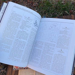 Pode incluir: Um livro aberto numa p&aacute;gina com instru&ccedil;&otilde;es para fazer um quilt de cesta floral, uma cesta de madeira e uma parede de cabana de troncos. O livro apresenta ilustra&ccedil;&otilde;es de cada projeto e lista os materiais necess&aacute;rios.