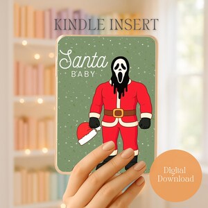 May include: A Kindle insert with a green background featuring a cartoon of a figure in a Santa Claus suit with a Scream mask. The text "Santa Baby" is displayed above the figure. A Santa hat is on the ground. The words "Kindle Insert" are at the top.