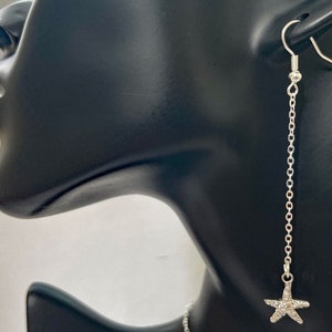 May include: Silver dangle earrings with a sparkly starfish charm hanging from a delicate chain.