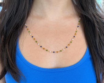 May include: A gold chain necklace with small, colorful beads. The beads are in a repeating pattern of green, blue, white, and orange.