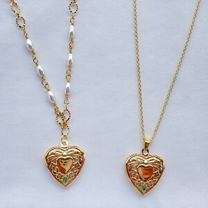 May include: Two gold heart-shaped locket necklaces. One necklace has a chain with white oval beads, the other has a simple gold chain.