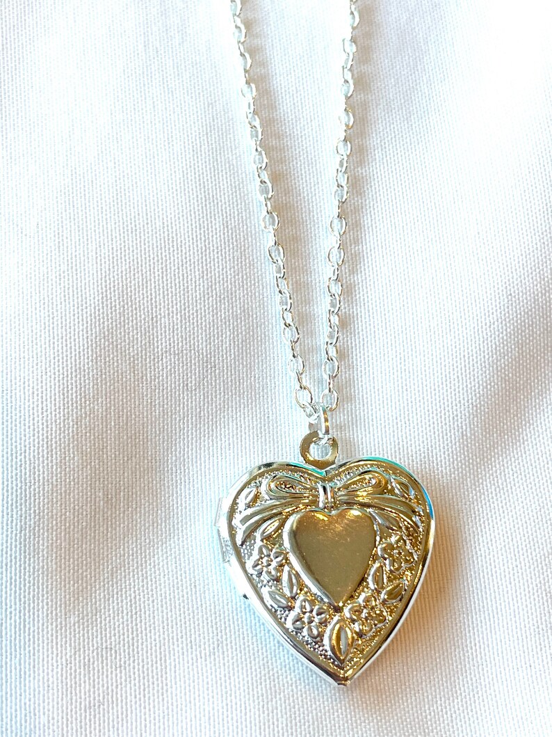 Peut inclure: Un collier avec un pendentif en forme de c&oelig;ur argent&eacute; et une cha&icirc;ne d&eacute;licate. Le pendentif pr&eacute;sente un motif complexe de fleurs et d'un n&oelig;ud.