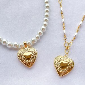 May include: Two gold heart-shaped lockets on necklaces. One necklace is a pearl strand and the other is a gold chain with pearl accents.