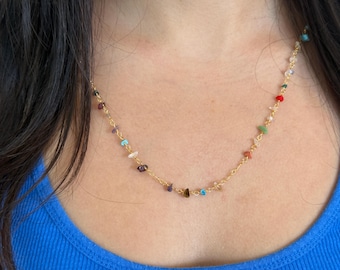 May include: A gold chain necklace with small, colorful gemstone beads. The necklace is delicate and features a variety of colors, including red, green, blue, and purple.