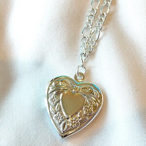 Peut inclure: Collier avec pendentif en forme de c&oelig;ur en argent, avec une cha&icirc;ne d&eacute;licate. Le pendentif pr&eacute;sente un motif floral complexe et un petit c&oelig;ur au centre.