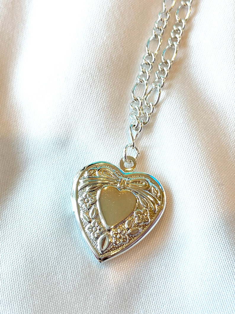 Peut inclure: Collier avec pendentif en forme de c&oelig;ur en argent, avec une cha&icirc;ne d&eacute;licate. Le pendentif pr&eacute;sente un motif floral complexe et un petit c&oelig;ur au centre.