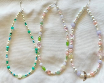 May include: Three beaded necklaces with different colored beads and charms. The necklaces are made with white, green, blue, and purple beads. The charms include butterflies and a heart.