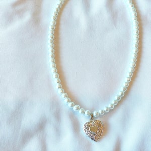 Peut inclure: Un collier de perles blanches avec un pendentif en forme de c&oelig;ur argent&eacute;.