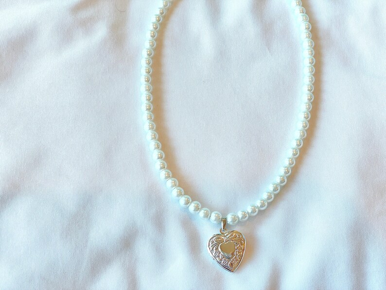 Peut inclure: Un collier de perles blanches avec un pendentif en forme de c&oelig;ur argent&eacute;.