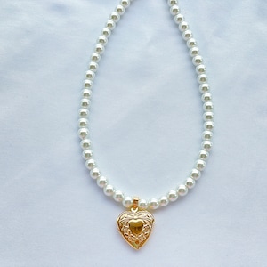 May include: A white pearl necklace with a gold heart-shaped locket pendant.