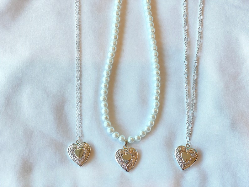 Peut inclure: Trois colliers en argent avec des pendentifs en forme de c&oelig;ur. Le collier de gauche a une cha&icirc;ne en argent, le collier du milieu a une cha&icirc;ne de perles et le collier de droite a une cha&icirc;ne en argent.