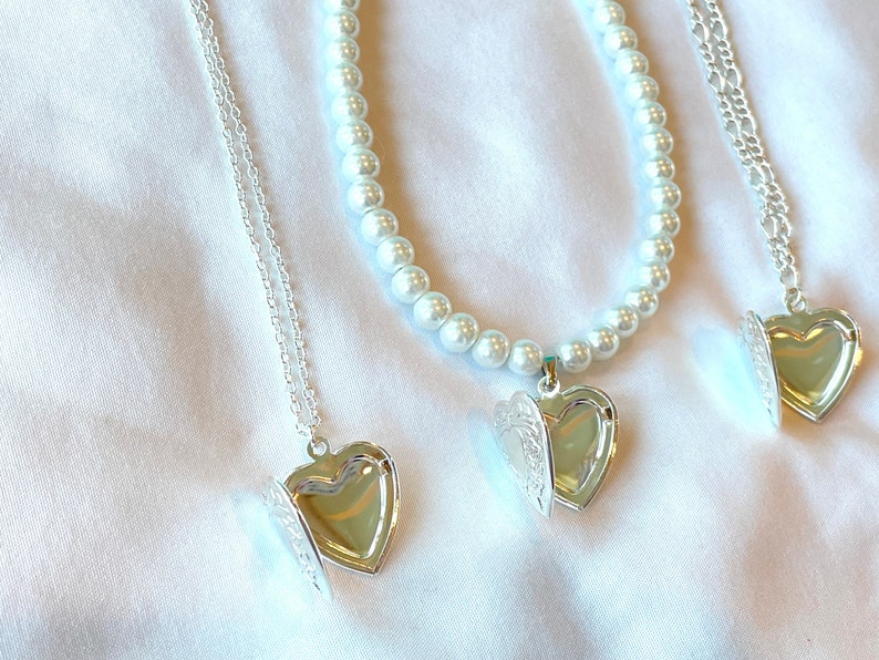 Peut inclure: Trois colliers avec un m&eacute;daillon en forme de c&oelig;ur argent&eacute;, l'un avec une cha&icirc;ne de perles et les deux autres avec des cha&icirc;nes argent&eacute;es. Les m&eacute;daillons sont ouverts, r&eacute;v&eacute;lant l'int&eacute;rieur.