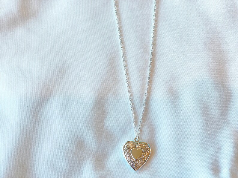 Peut inclure: Un collier avec un pendentif en forme de c&oelig;ur argent&eacute; orn&eacute;. Le pendentif a une petite ouverture en forme de c&oelig;ur au centre.