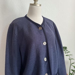 May include: A navy blue cardigan with a round neckline and dark blue trim. The cardigan has three silver-coloured buttons and two front pockets. The garment is displayed on a mannequin.